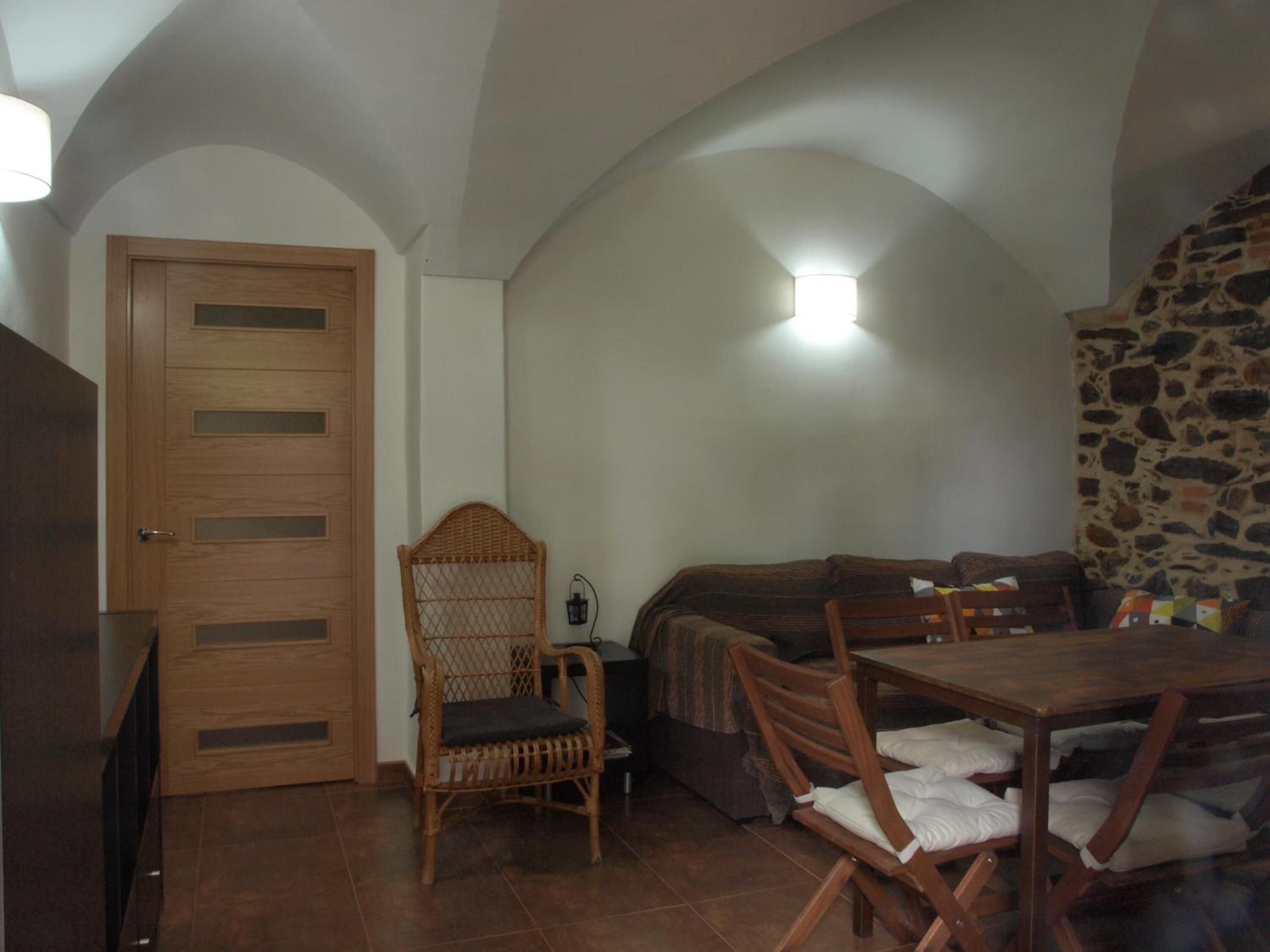 Una habitación acogedora con puerta de madera, una silla de mimbre, un sofá y una mesa de comedor con sillas.