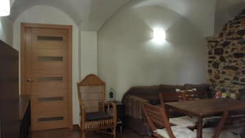 Una habitación acogedora con puerta de madera, una silla de mimbre, un sofá y una mesa de comedor con sillas.