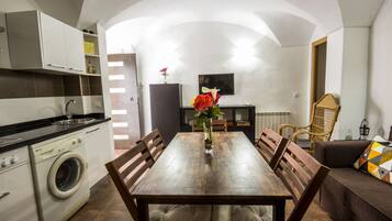 A compact kitchen with a washing machine, a dining table with chairs, and a living area with a sofa and a TV.
