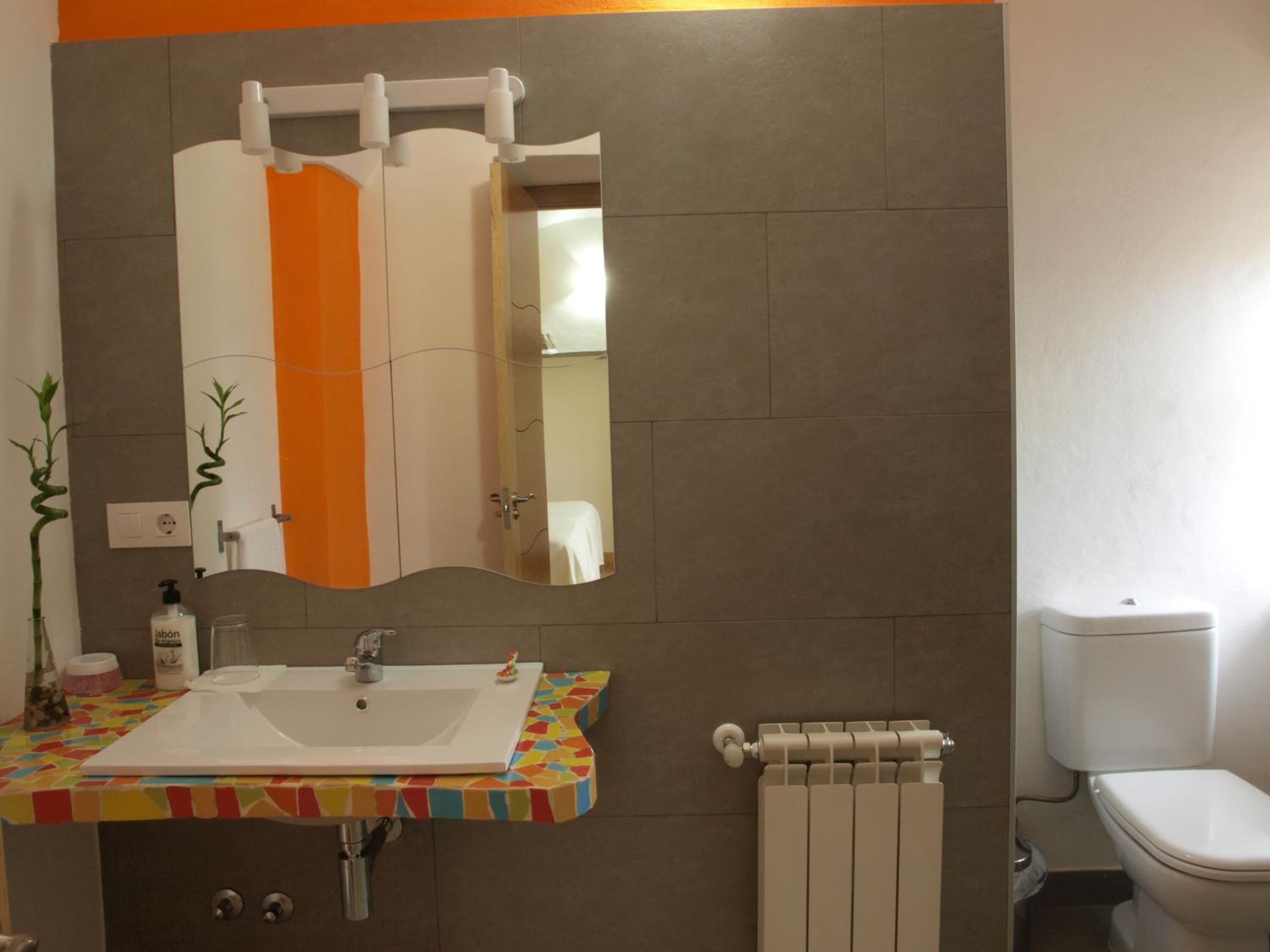 A bathroom with a white sink, a mirror with an orange stripe, a radiator, and a toilet.