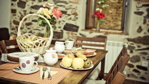 Una mesa de madera con un cesto de pan, un plato de fruta y una taza de té.