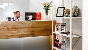 A reception desk with a wooden counter, a computer, and a shelf with brochures and a vase of flowers. - Duvan Hotell (Uppsala)