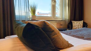 A bedroom with a bed, a window with curtains, a potted plant, and a view of a building outside. - Duvan Hotell (Uppsala)