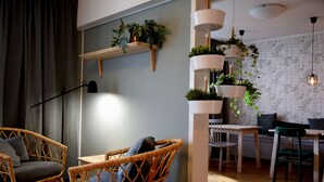 A cozy room with wicker chairs, a wooden table, and a dining area. There are hanging plants and a lamp. - Duvan Hotell (Uppsala)