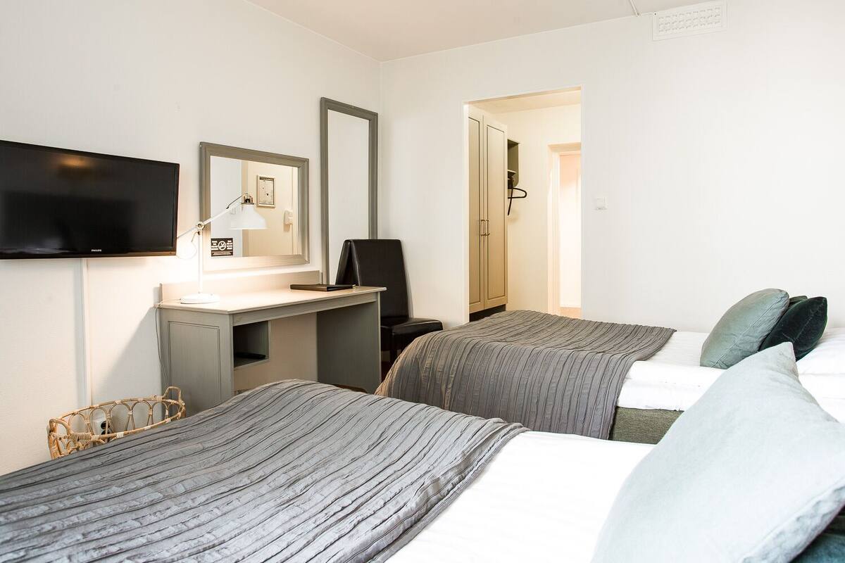 Ett hotellrum med två sängar, ett skrivbord, en stol, en tv och en garderob.