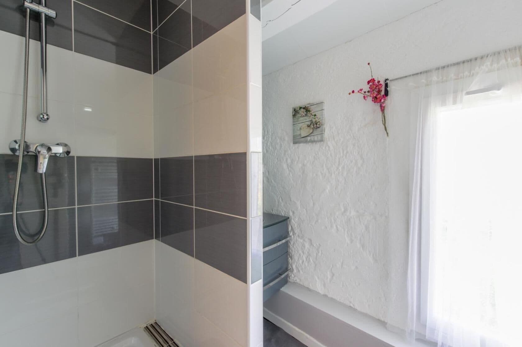 A bathroom with a shower, a bathtub, and a window with curtains.