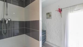 A bathroom with a shower, a bathtub, and a window with curtains.