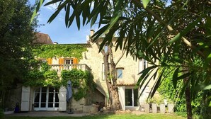 A stone building with a covered patio, surrounded by a well-maintained lawn and trees. - Clos de la Colombe (Pouzols)
