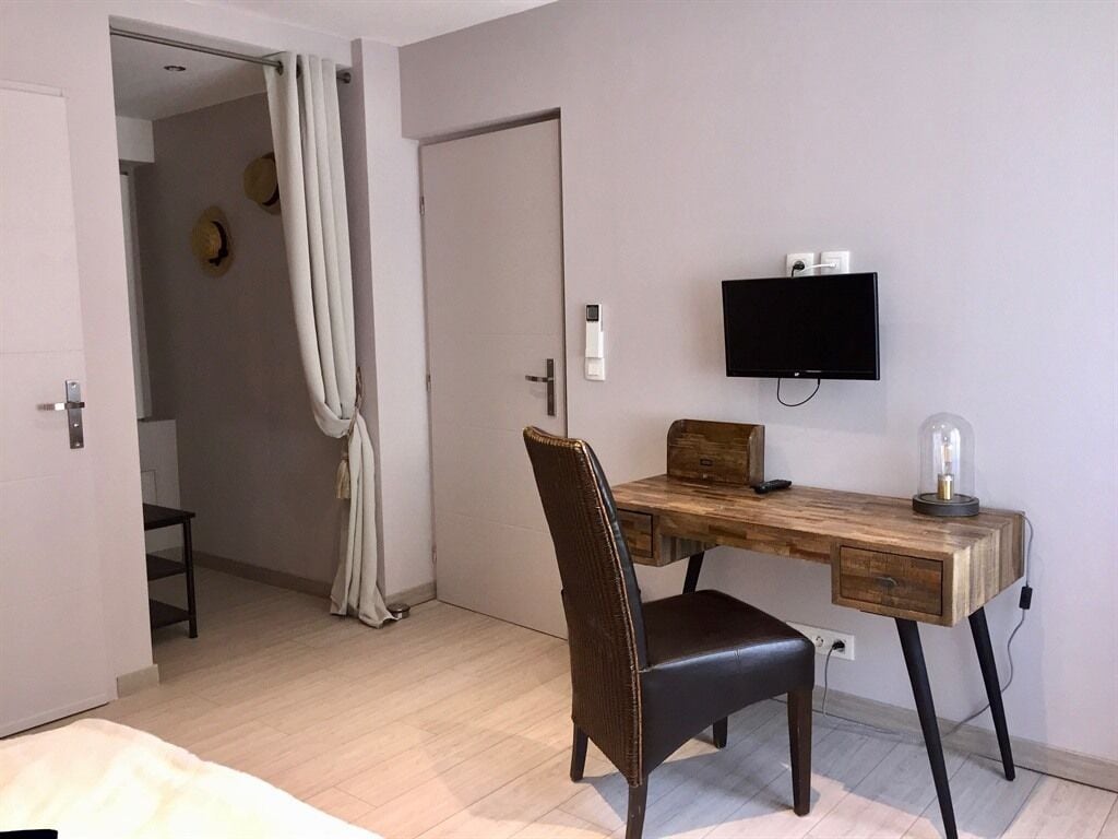 Een slaapkamer met een houten bureau, een stoel, een televisie en een nachtkastje.