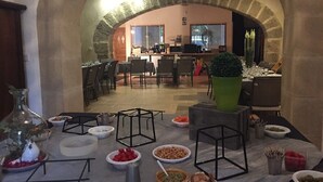 A dining area with a stone archway, tables set with various dishes, and a view into the kitchen area. - Clos de la Colombe (Pouzols)