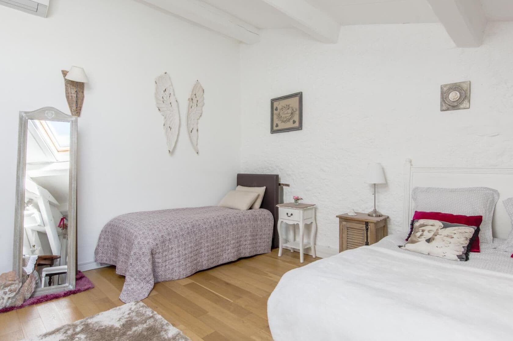 Een slaapkamer met een bed, nachtkastje, dressoir, spiegel en decoratieve objecten aan de muur.
