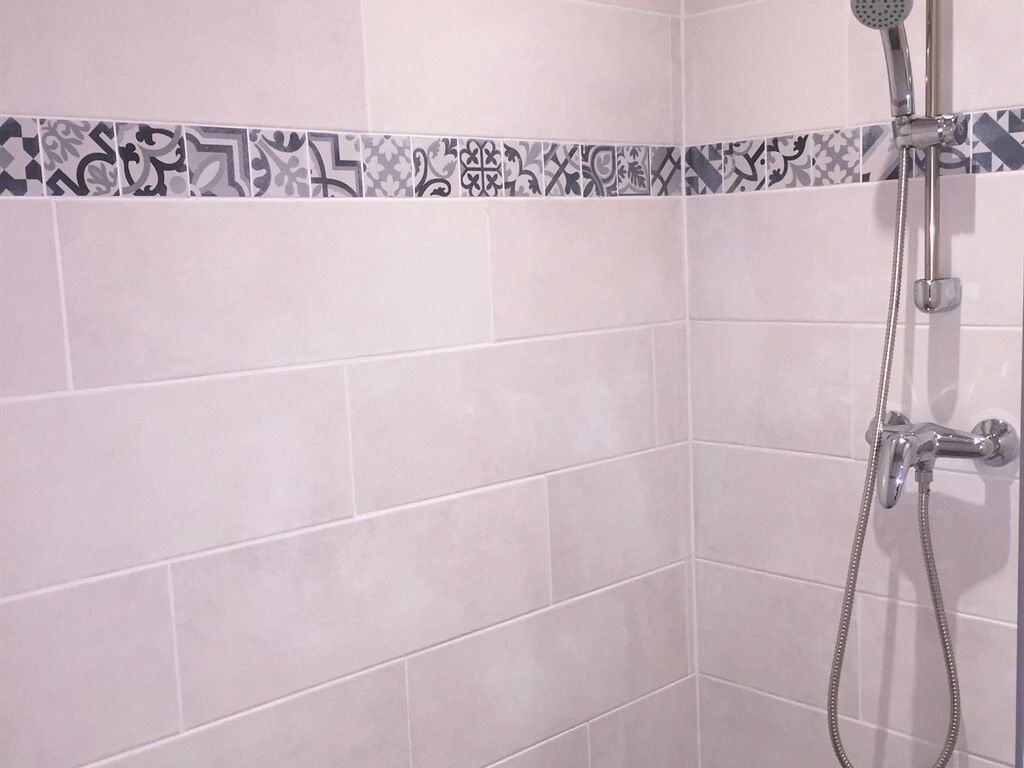Zona de ducha con pared de azulejos, cabezal de ducha y ducha de mano.