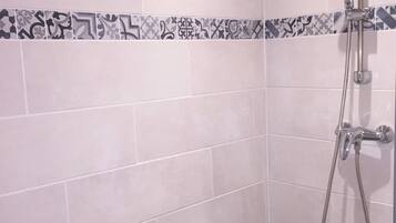 Zona de ducha con pared de azulejos, cabezal de ducha y ducha de mano.