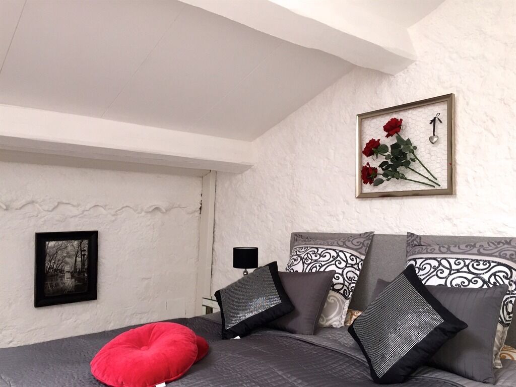 Een slaapkamer met een bed, kussens, een lijst met bloemen en een nachtkastje met een lamp.