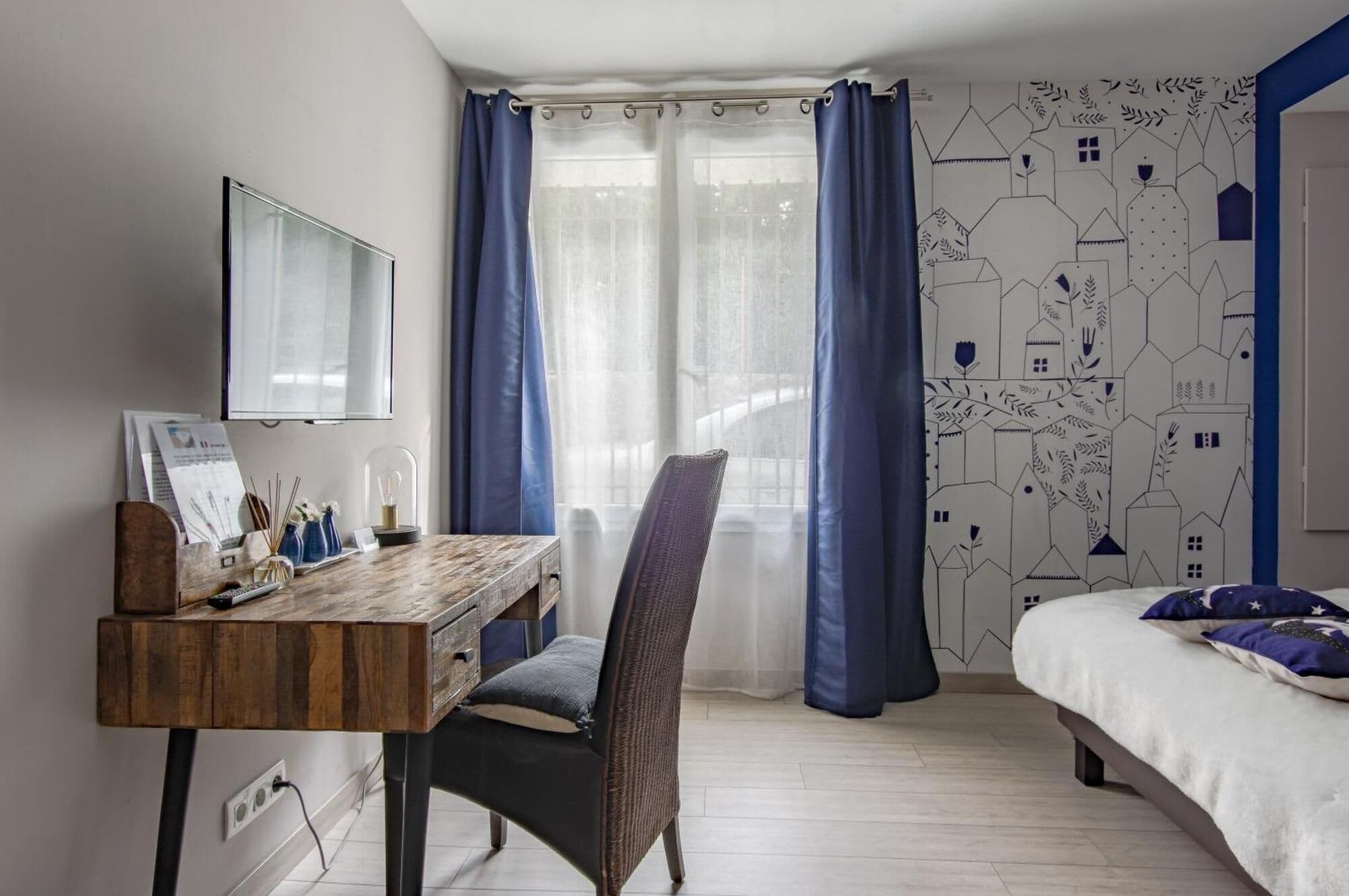 Un dormitorio con cama, escritorio con silla, televisión y ventana con cortinas.