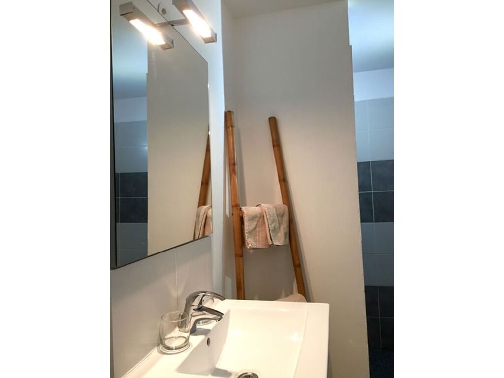 A bathroom with a white sink, mirror, and wooden ladder leaning against the wall.