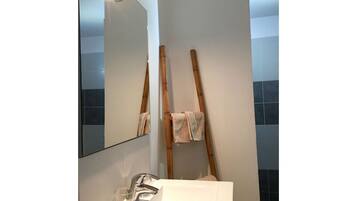 A bathroom with a white sink, mirror, and wooden ladder leaning against the wall.