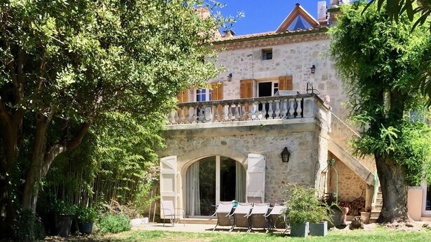 A stone building with a balcony, arched entrance, and outdoor seating area. - Clos de la Colombe (Pouzols)
