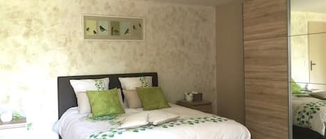 A bedroom with a bed, a nightstand, a mirror, and a wall-mounted picture frame.