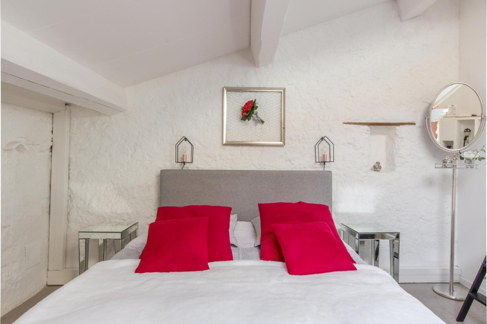 Un dormitorio moderno con una cama grande, dos mesitas de noche, un espejo y un cuadro enmarcado en la pared.