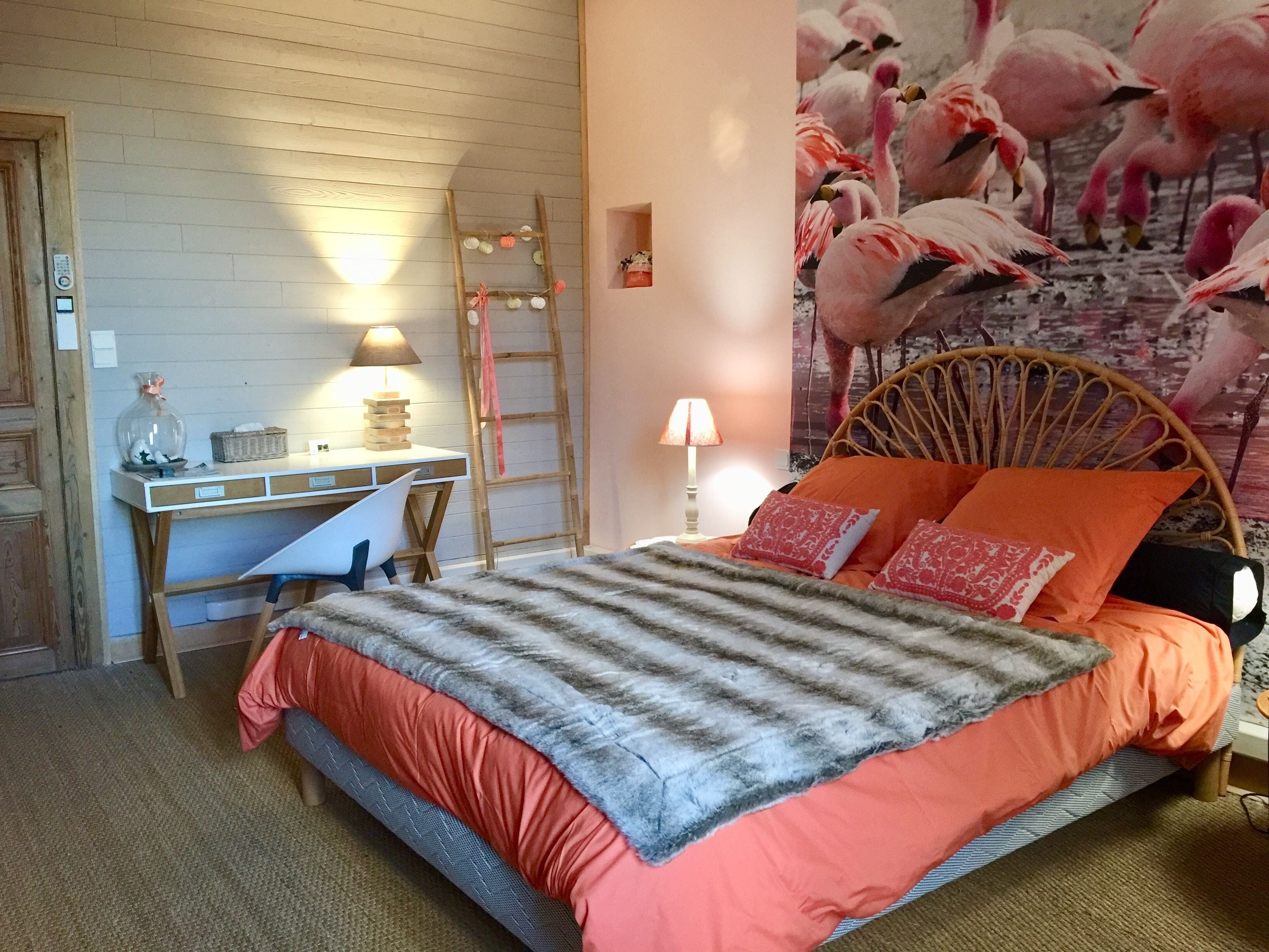 Makuuhuoneessa on sänky, työpöytä, tuoli, tikkaat ja seinä, jossa on flamingoaiheinen seinämaalaus.