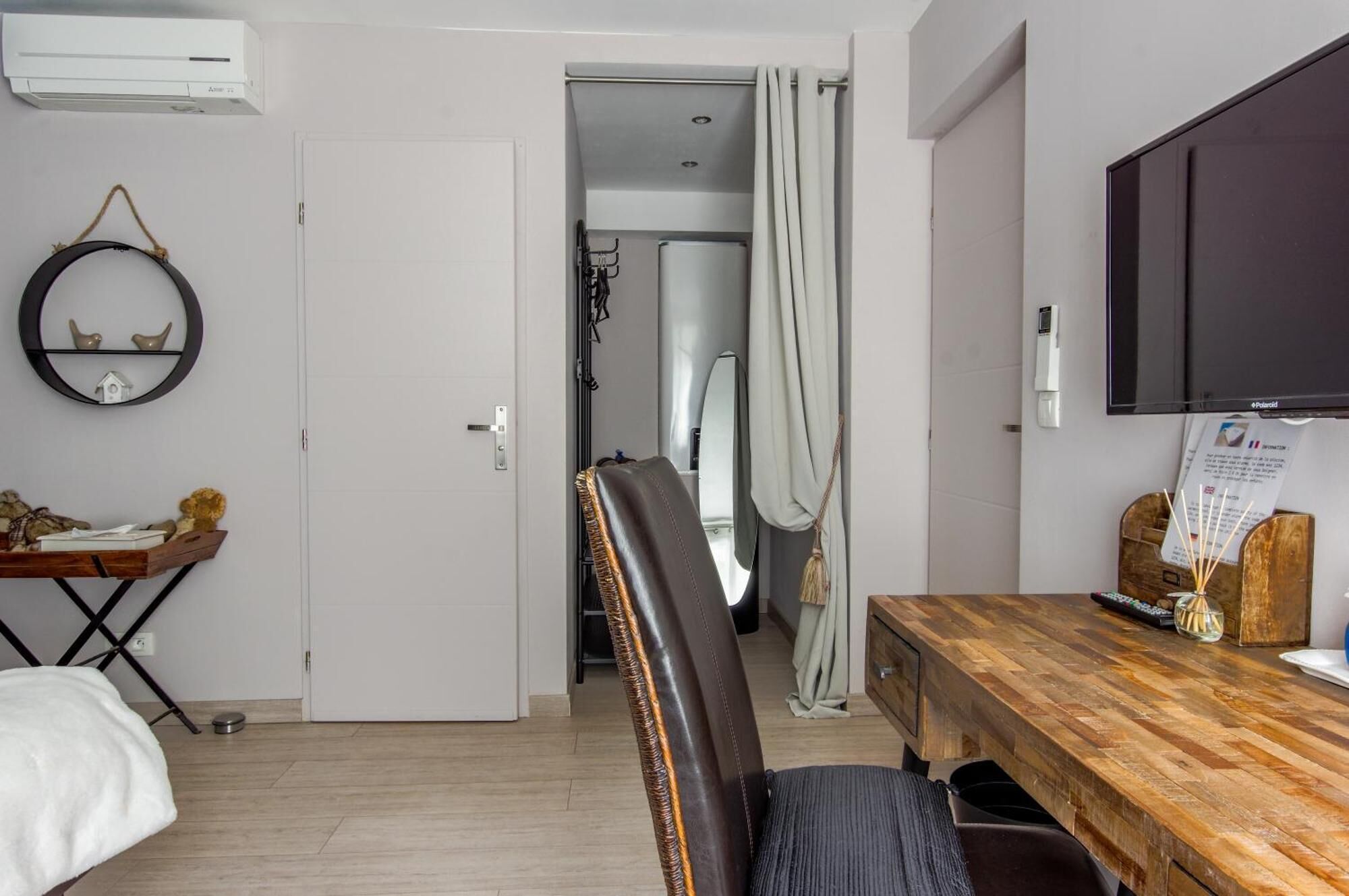 Habitación de hotel con cama, una mesa de comedor de madera, televisor, aire acondicionado instalado en la pared y una puerta que da a otra habitación.