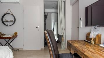 Habitación de hotel con cama, una mesa de comedor de madera, televisor, aire acondicionado instalado en la pared y una puerta que da a otra habitación.