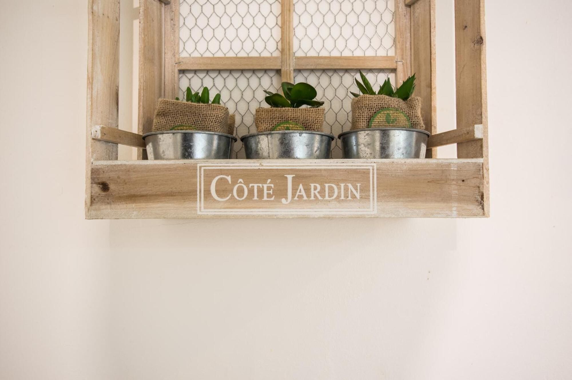Una estantería de madera con tres macetas de metal y una etiqueta que dice "Côté Jardin".