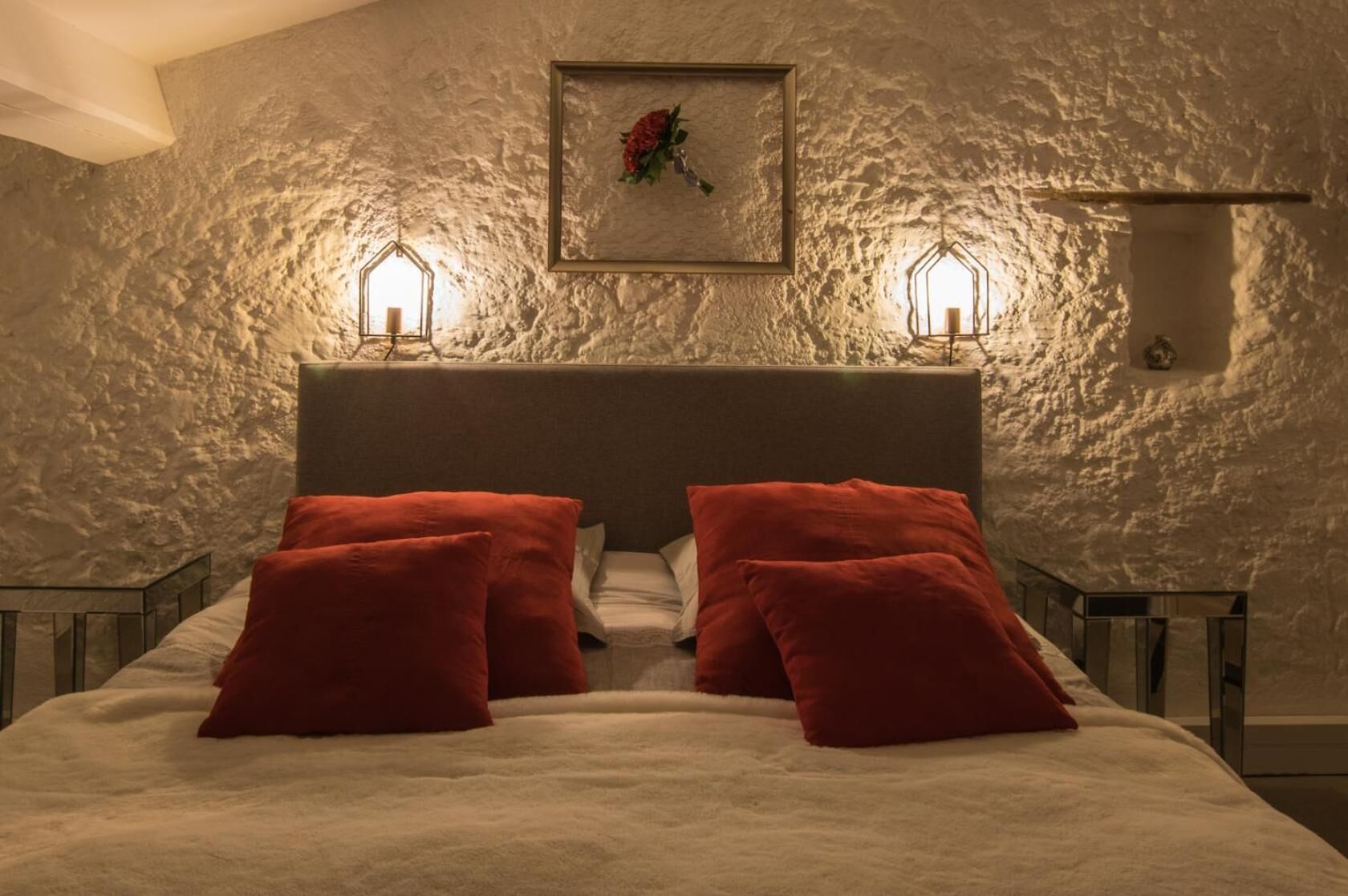Un dormitorio con pared de piedra texturizada, cabecera de madera y dos lámparas de noche.