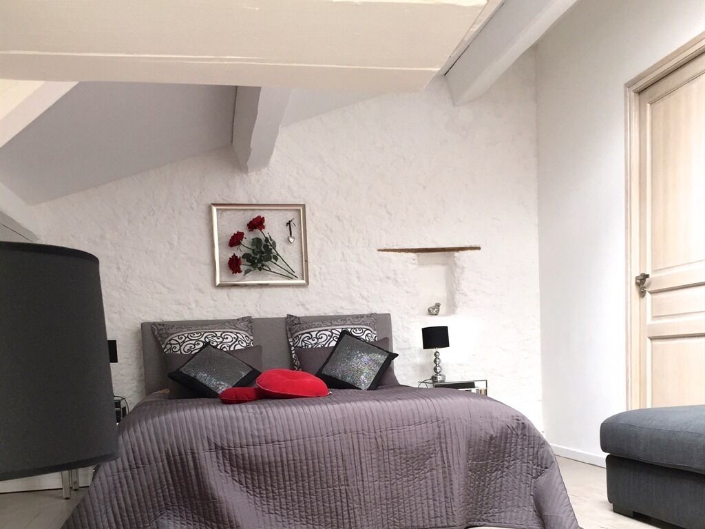 Un dormitorio con una cama, una mesita de noche, una lámpara, un cuadro en la pared y una puerta.