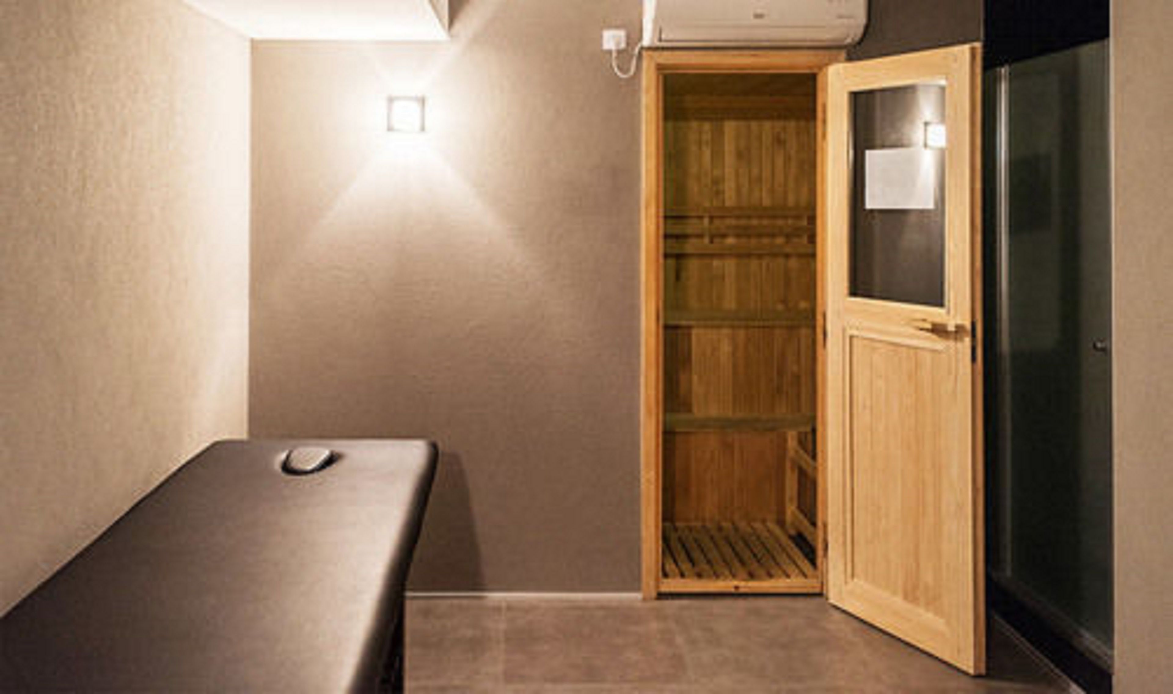 A room with a massage table, a wooden wardrobe, and a glass door.