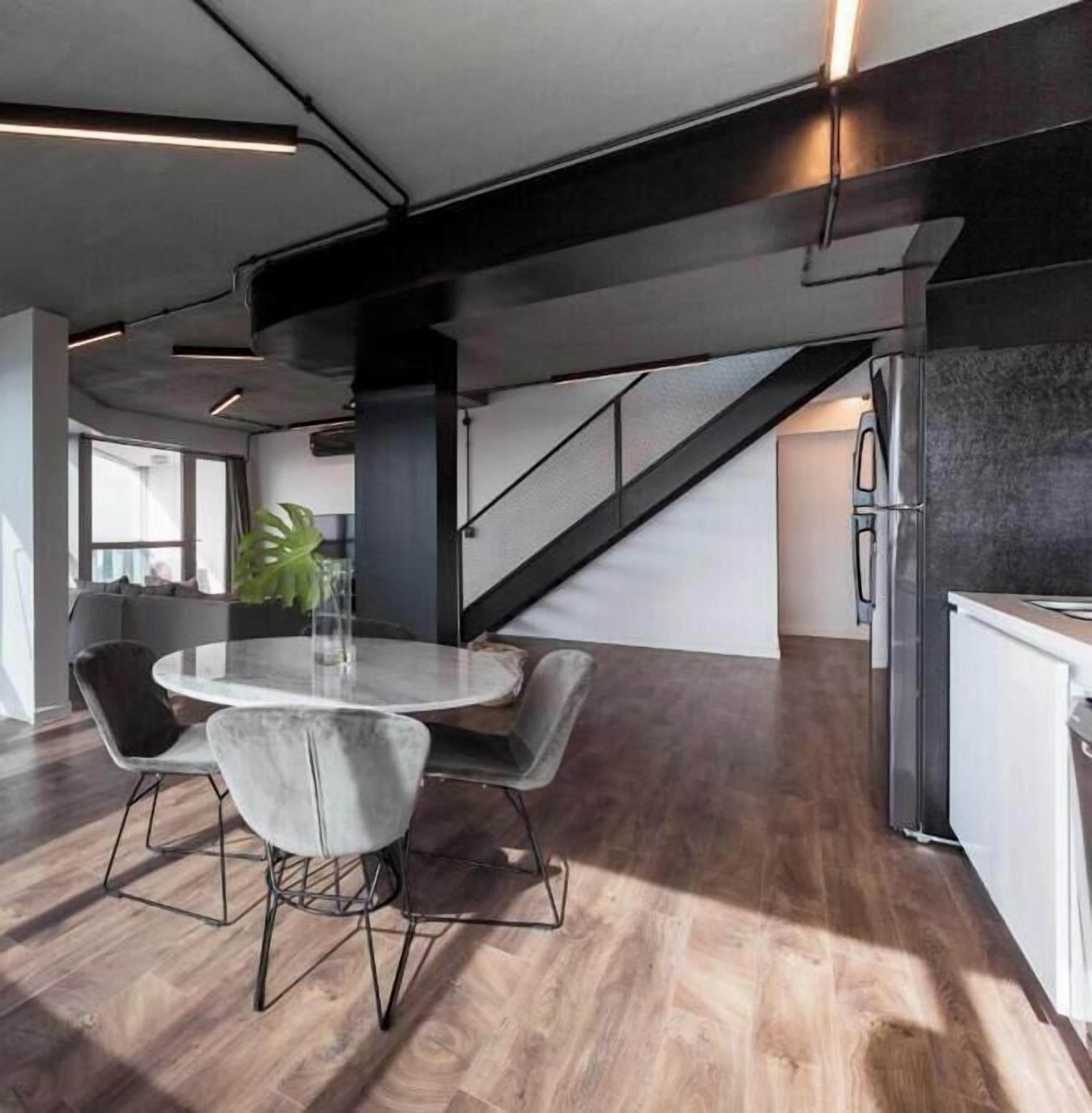 Una cocina moderna con refrigerador integrado, un comedor con mesa y sillas redondas, y una escalera que conduce a otro nivel.
