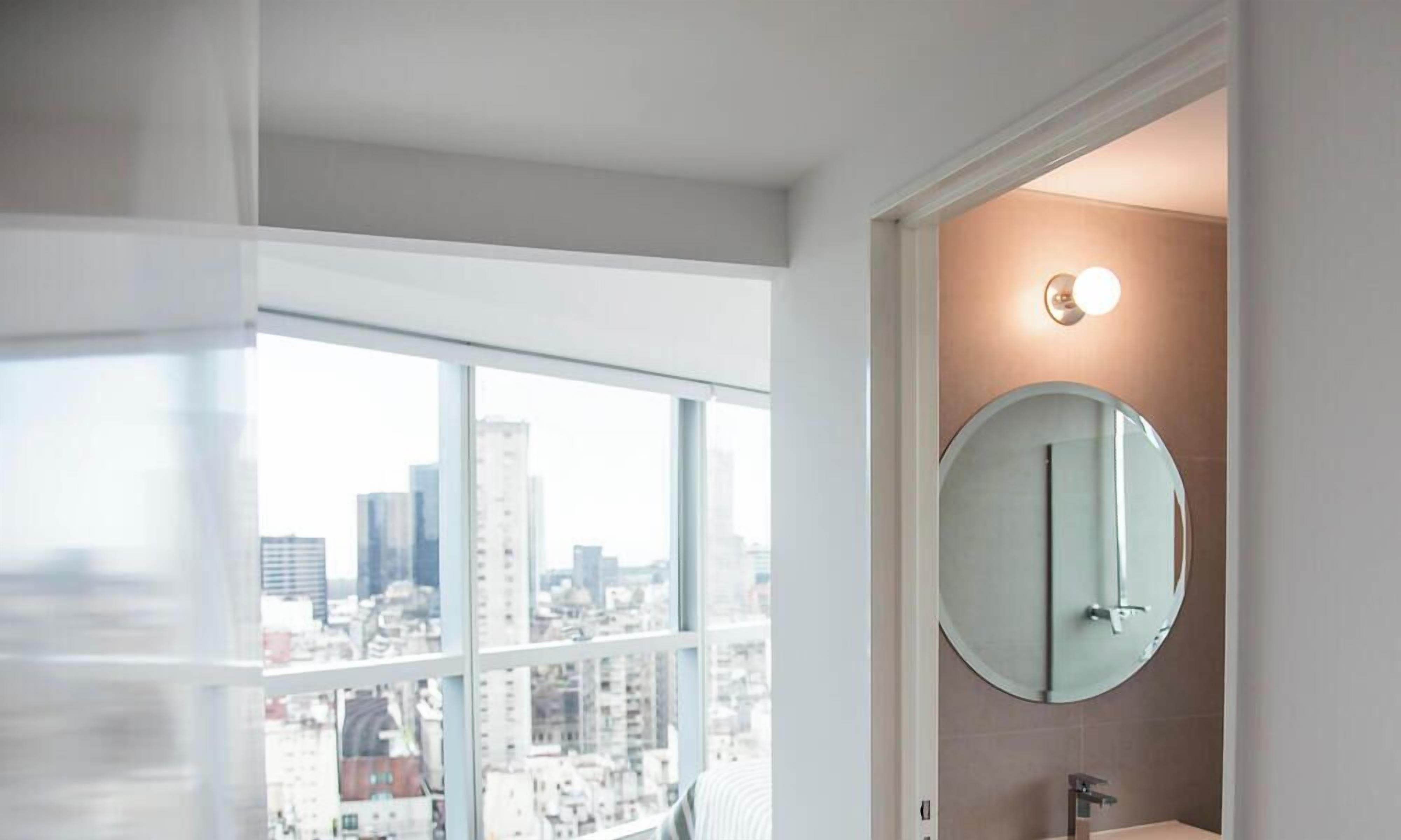 Un bagno moderno con un'ampia finestra, uno specchio rotondo e vista sulla città.