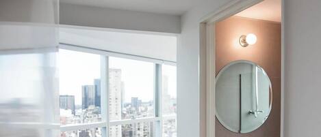 Un bagno moderno con un'ampia finestra, uno specchio rotondo e vista sulla città.