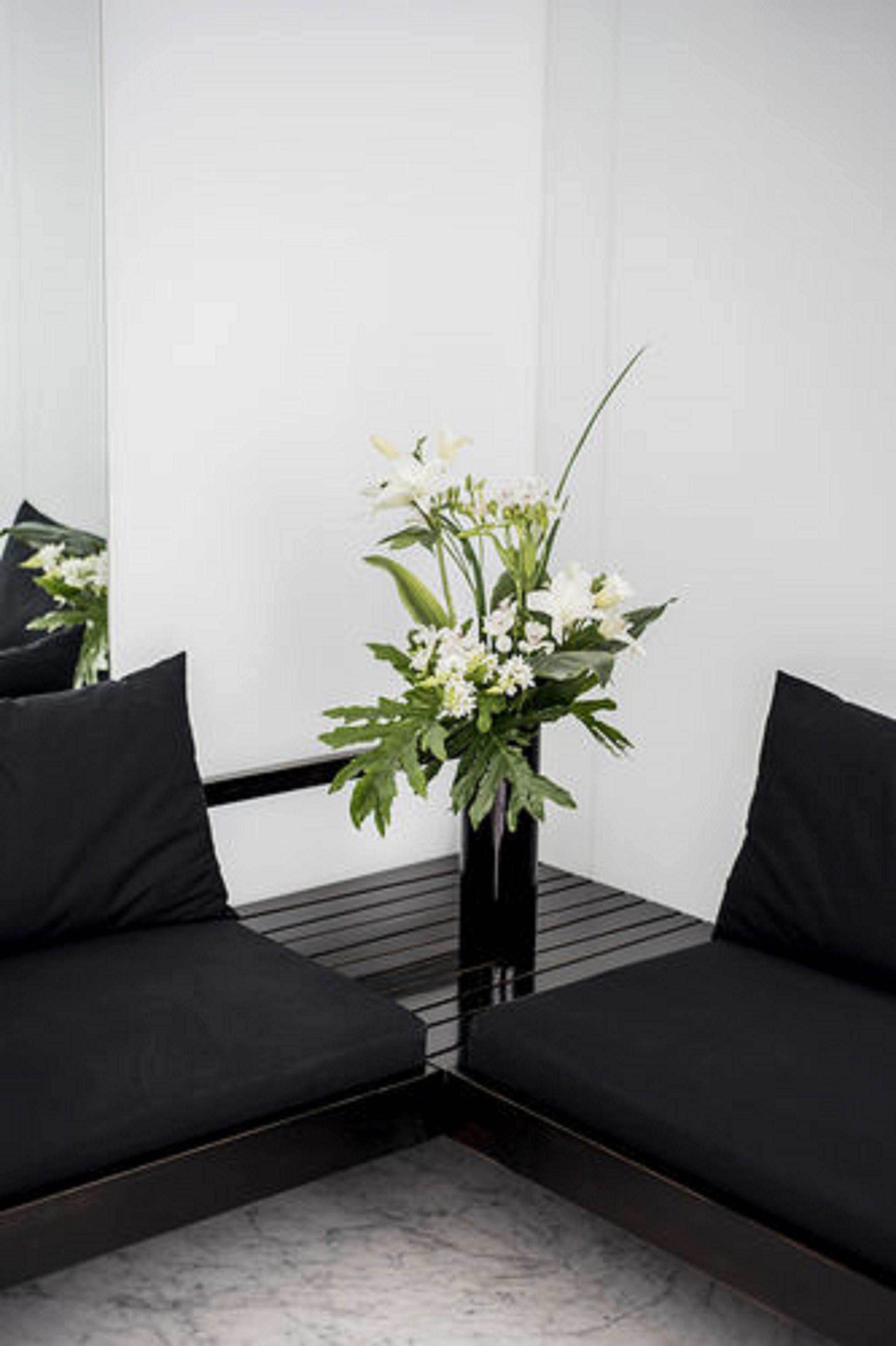 Et hjørnesæde med sorte polstrede stole og en sort vase med hvide blomster.