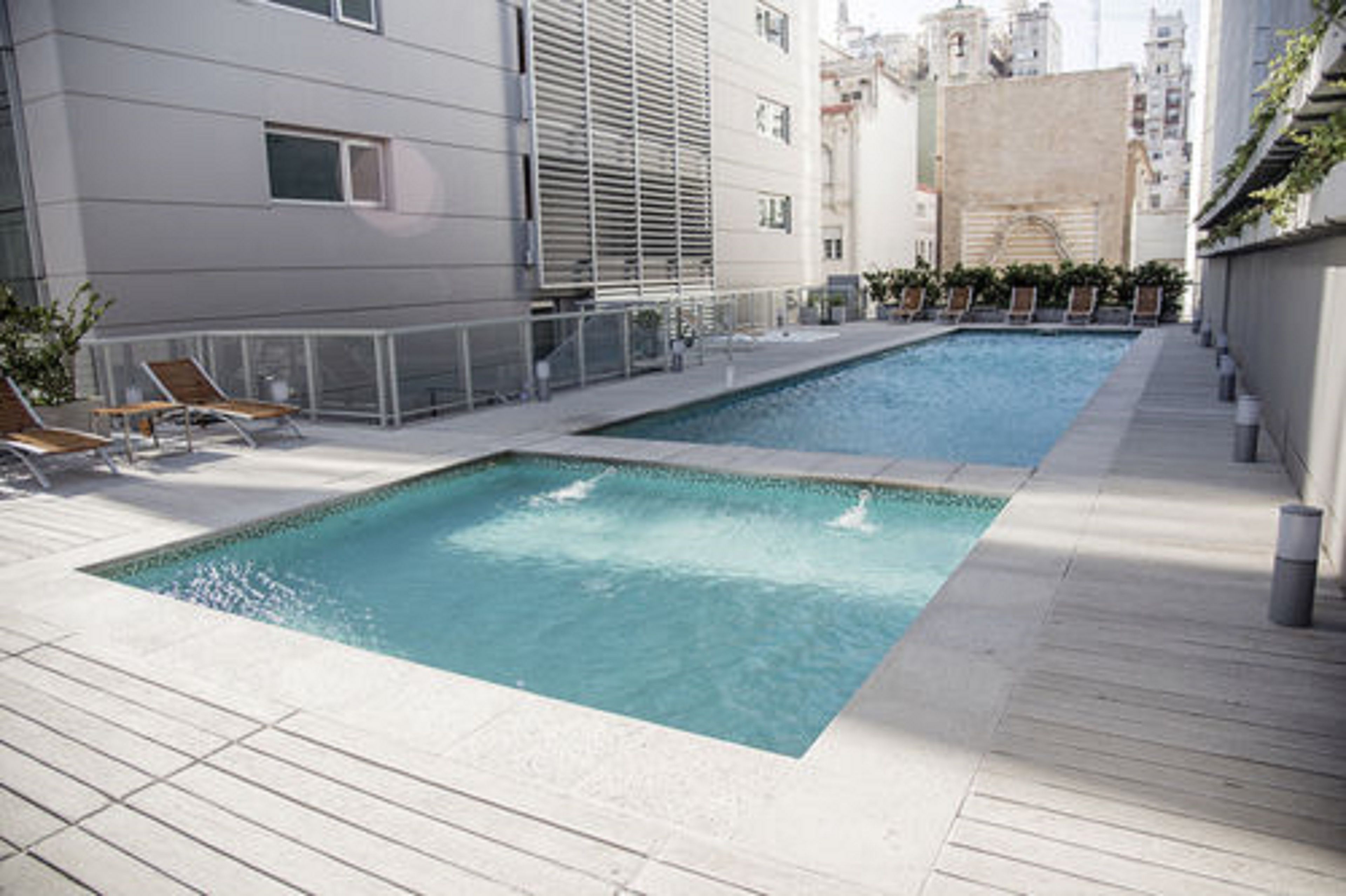 Una piscina en la azotea con dos zonas separadas, rodeada por una terraza de madera y una barandilla de metal.