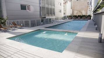 Una piscina en la azotea con dos zonas separadas, rodeada por una terraza de madera y una barandilla de metal.