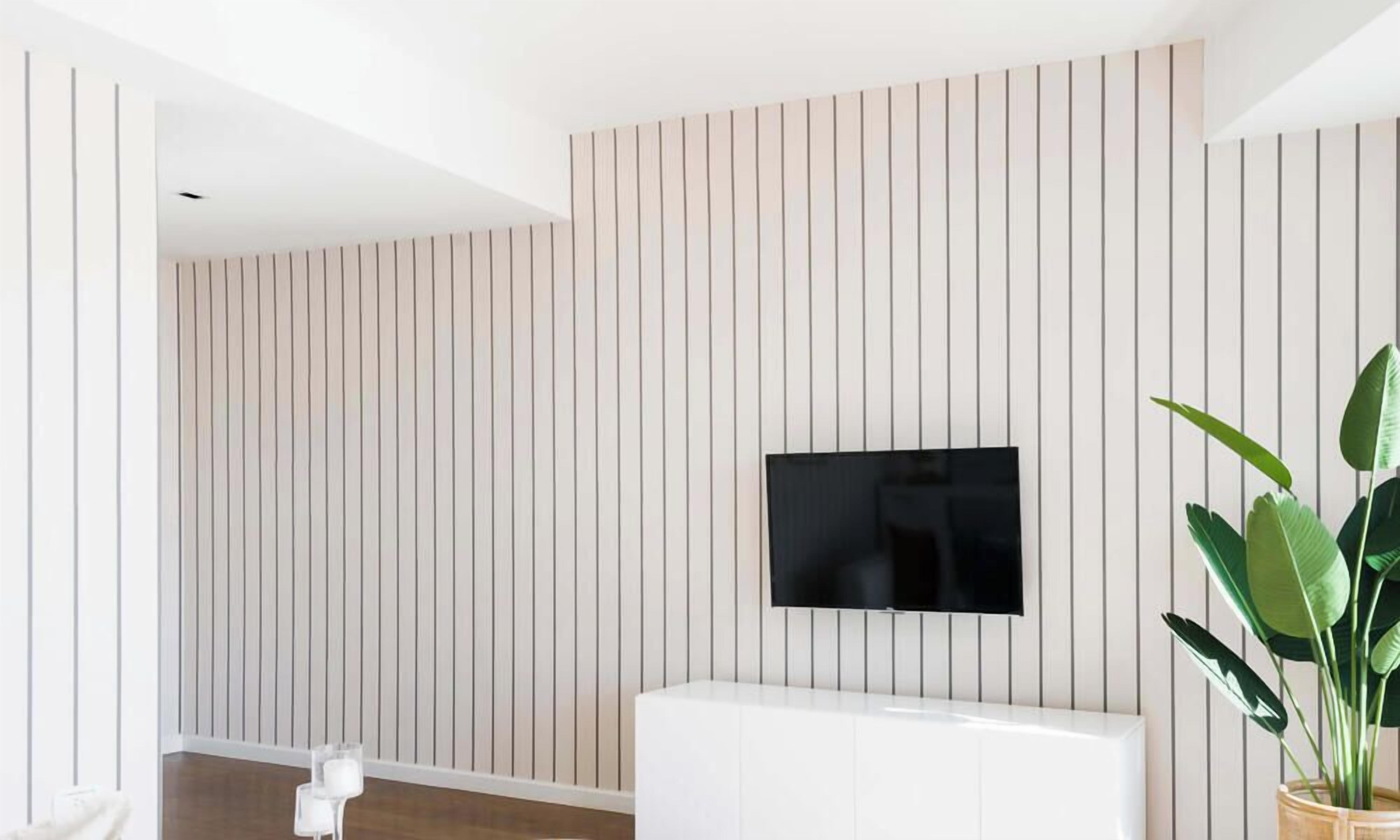 A modern living room with a flat-screen TV mounted on a wall with vertical paneling, a white entertainment unit, and a potted plant.