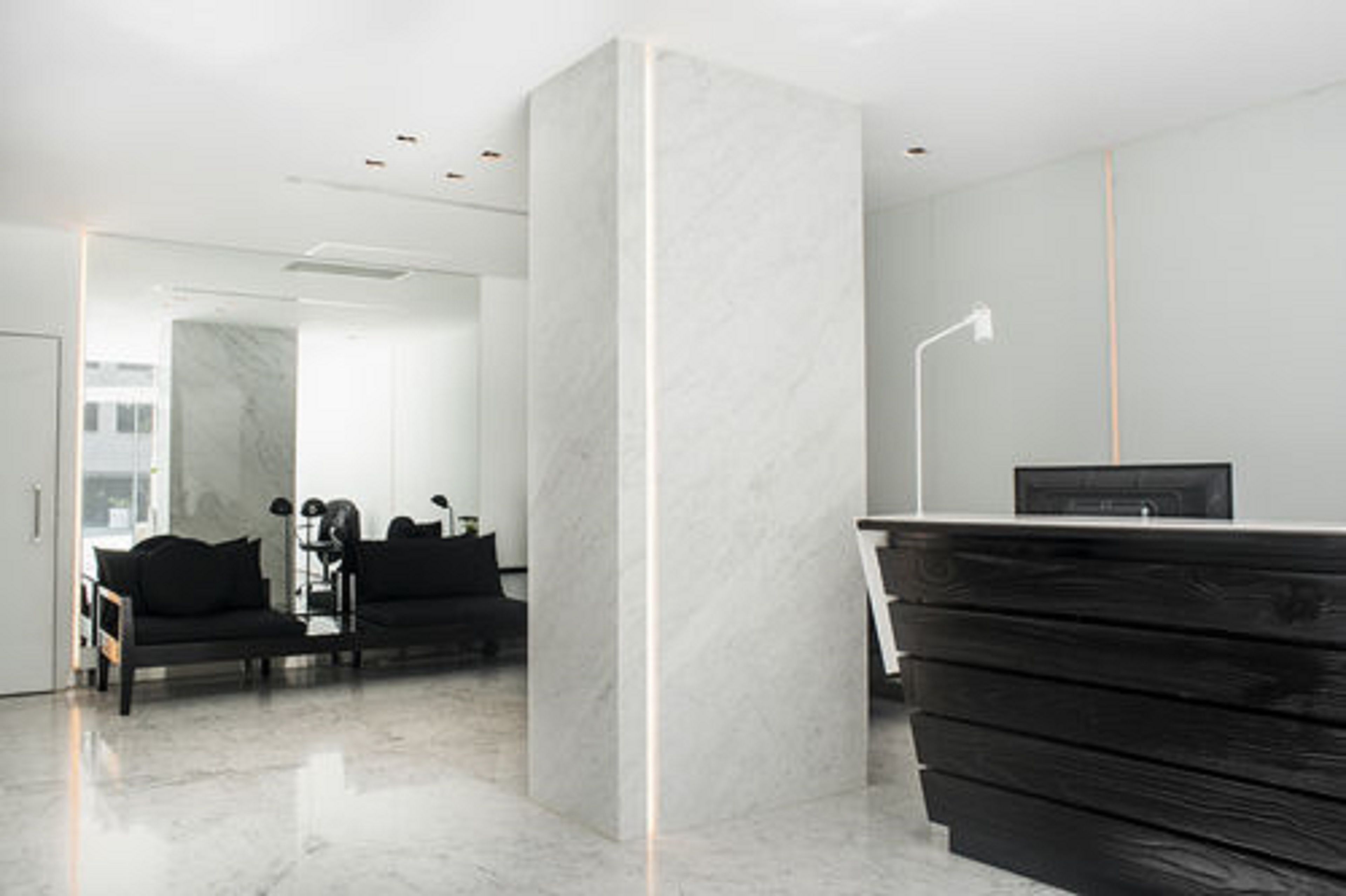 A modern reception area with a marble column, black furniture, and a flat-screen TV on a wooden desk.