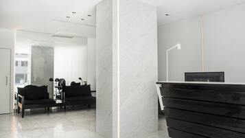 A modern reception area with a marble column, black furniture, and a flat-screen TV on a wooden desk.