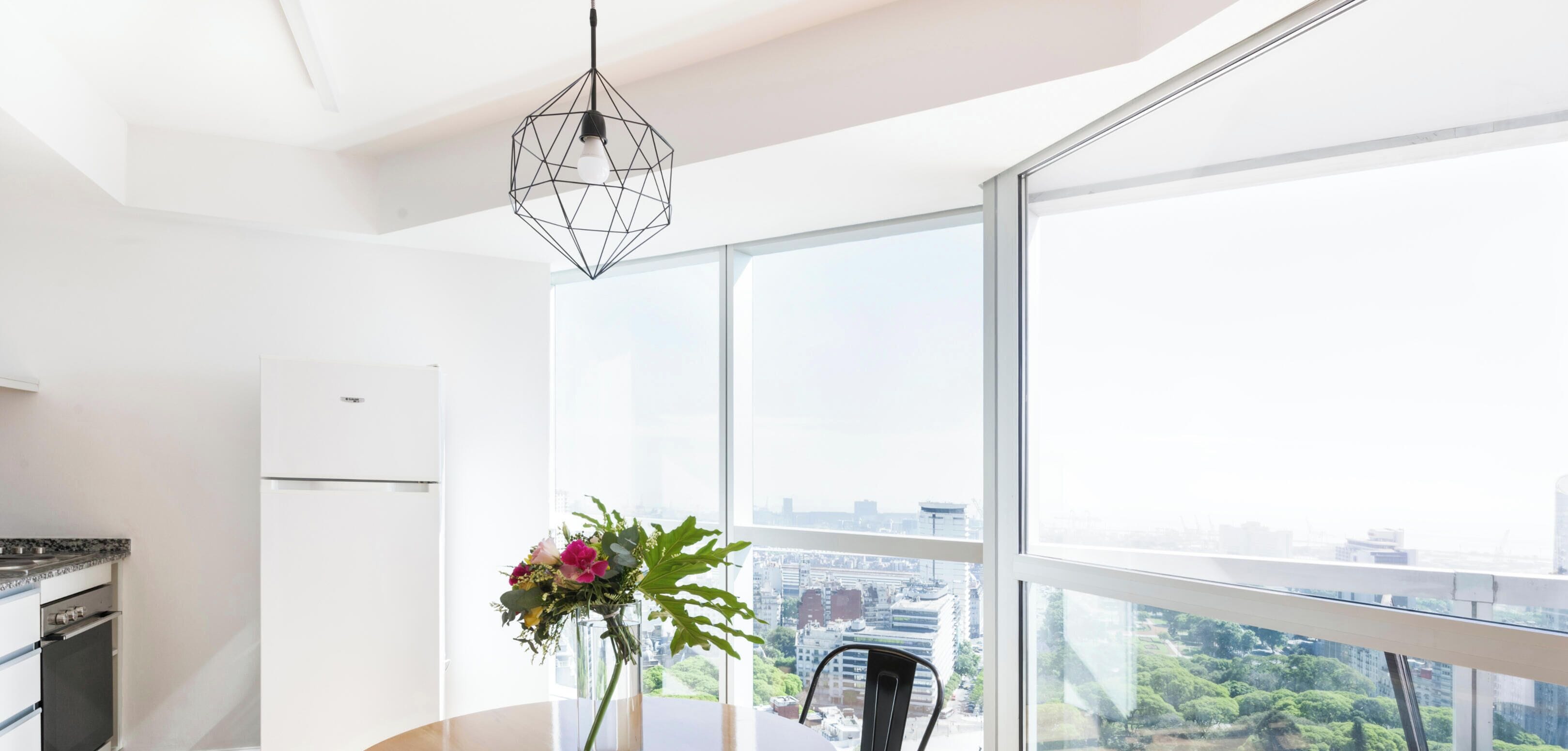 A modern kitchen with a built-in oven, a dining area with a table and chairs, and a large window offering a city view.