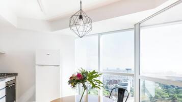 Een moderne keuken met een ingebouwde oven, een eethoek met een tafel en stoelen, en een groot raam met uitzicht op de stad.