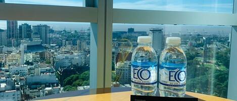 Un letrero de bienvenida con dos botellas de agua sobre una mesa, con vistas a un paisaje urbano a través de amplias ventanas.