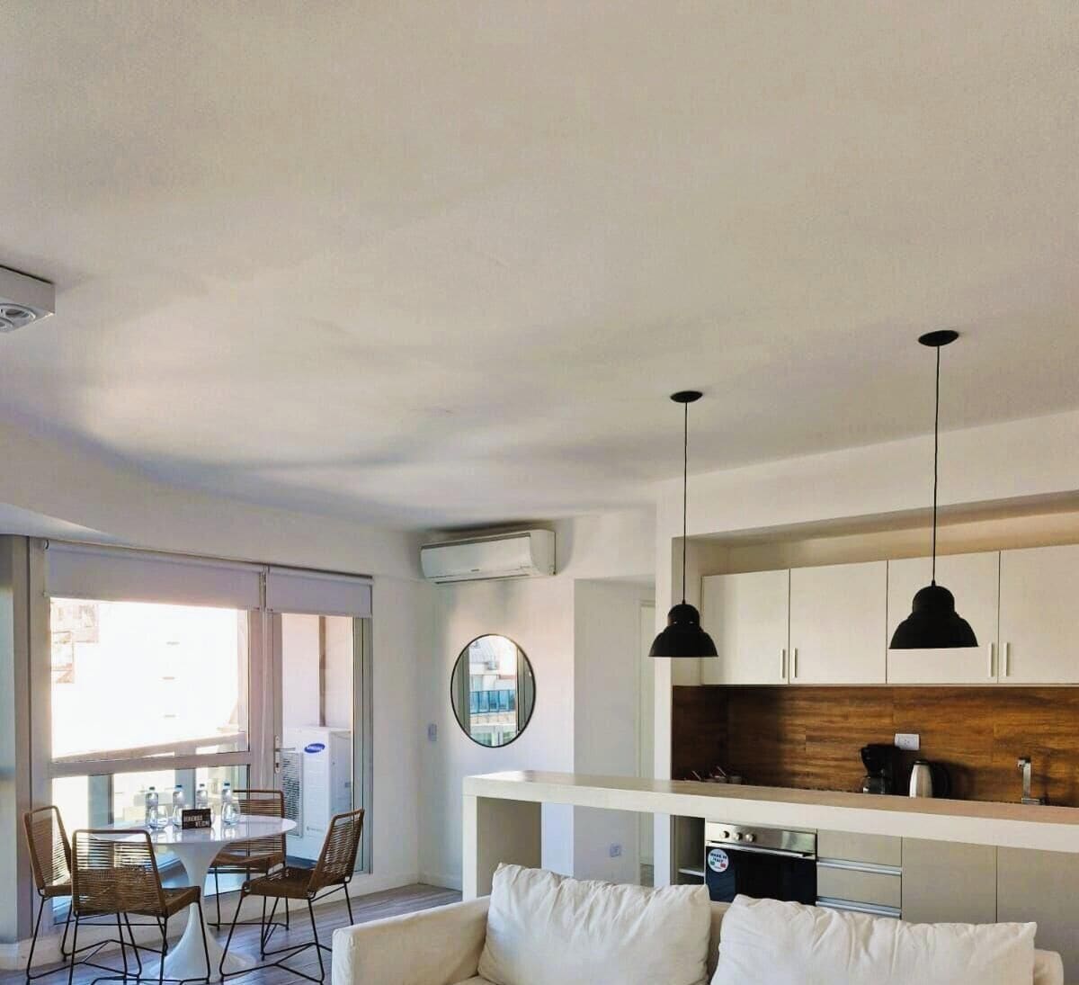 Una sala de estar moderna con sofá, mesa de comedor, sillas e iluminación colgante.