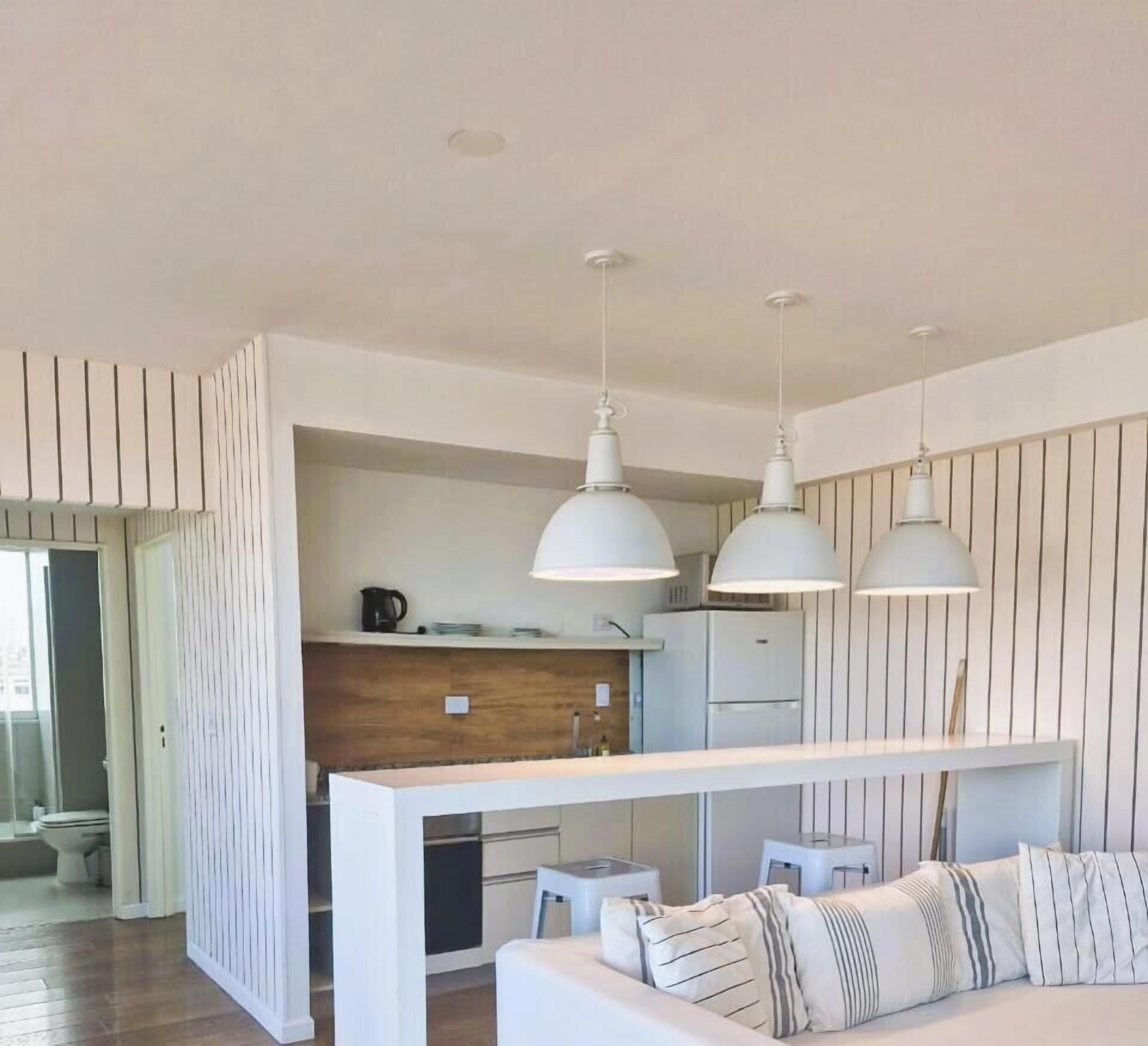 A modern kitchen with pendant lighting, a central island, and a seating area with striped cushions.