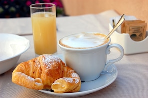 A breakfast setting with a croissant, a cup of coffee, and a glass of orange juice on a table.