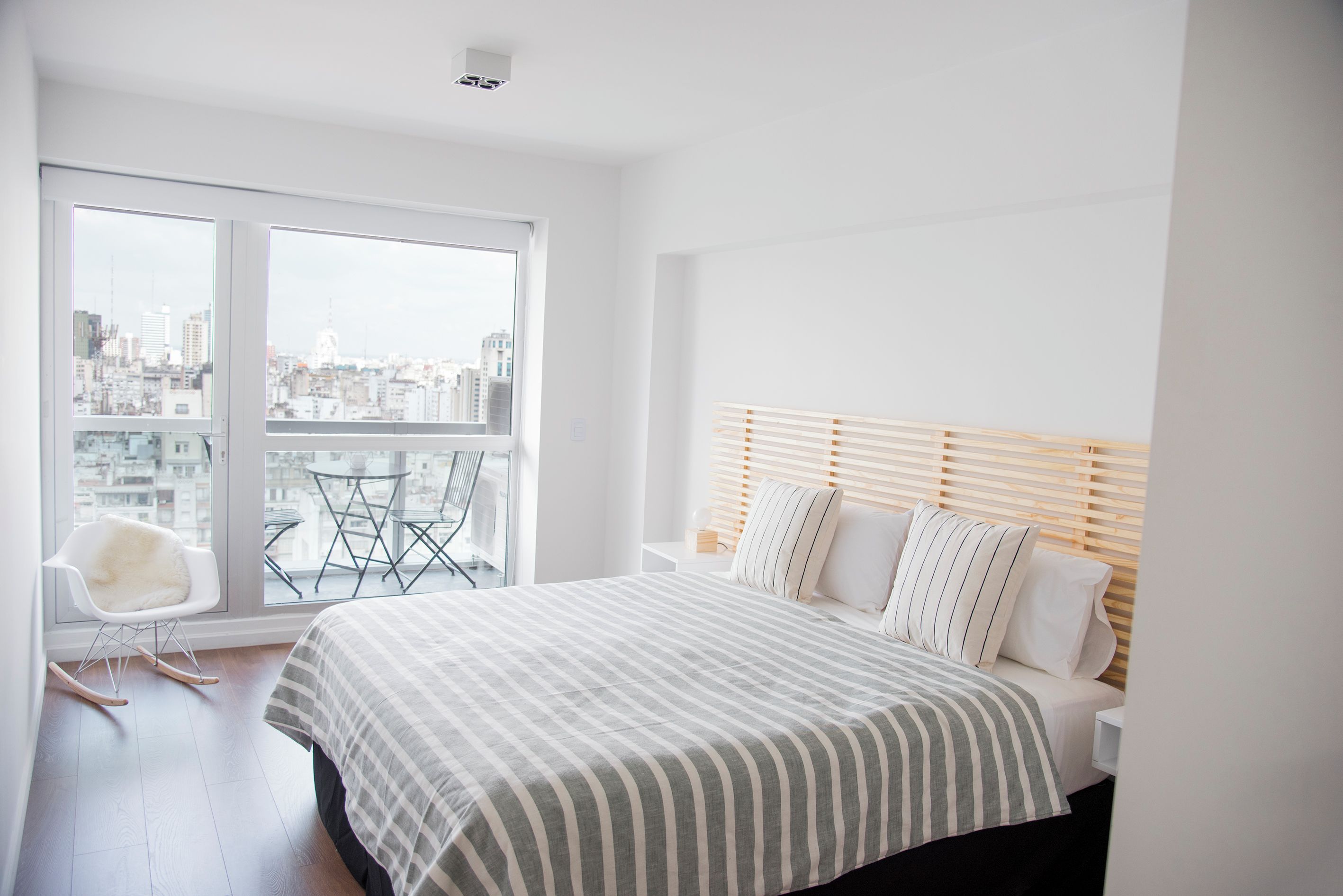 A modern bedroom with a large bed, a city view balcony, and a white color scheme.