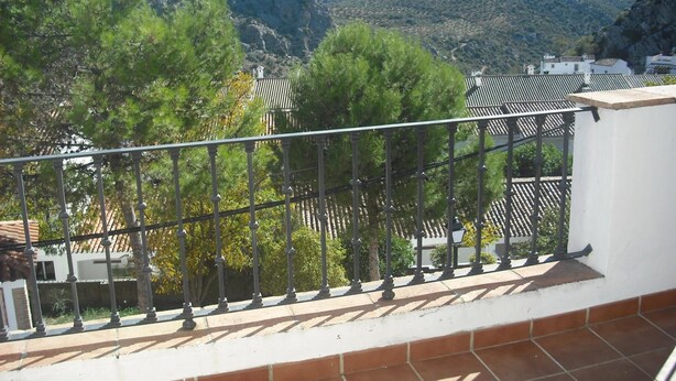 A balcony with a metal railing overlooking a mountainous landscape with trees and buildings. - Apartamentos Sierra del Hacho (Montejaque)