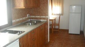 A kitchen with wooden cabinets, a double sink, and a refrigerator. - Apartamentos Sierra del Hacho (Montejaque)