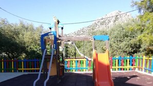 A playground with a slide and climbing structures, surrounded by a colorful fence and trees. - Apartamentos Sierra del Hacho (Montejaque)